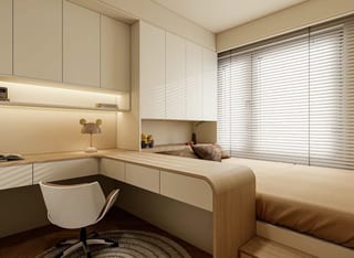A timber study desk beside a window and bed, with cream overhead cabinetry